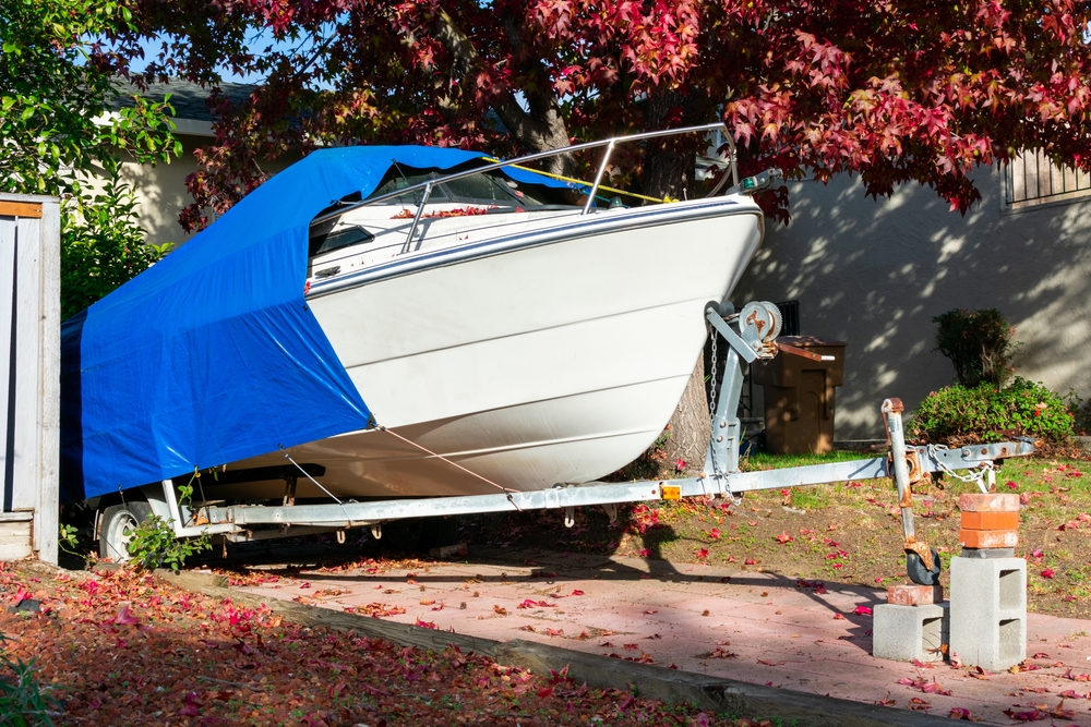 boat on trailer in a driveway, being half covered, showing only the front
