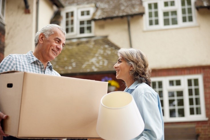happy older couple moving, man is holding a box and the woman is holding a lamp