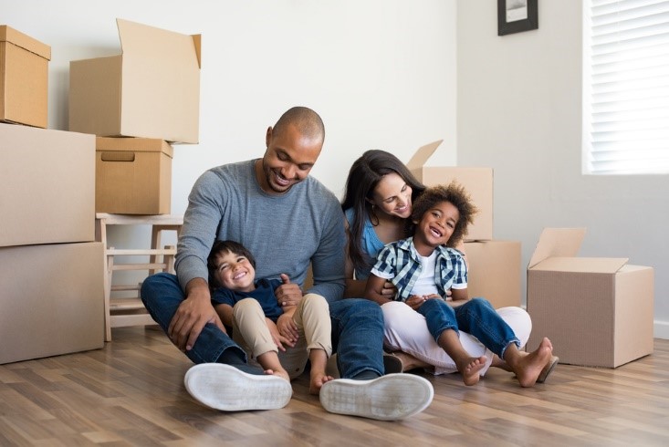 family recently moved in, happy and sitting on floor with boxes behind them