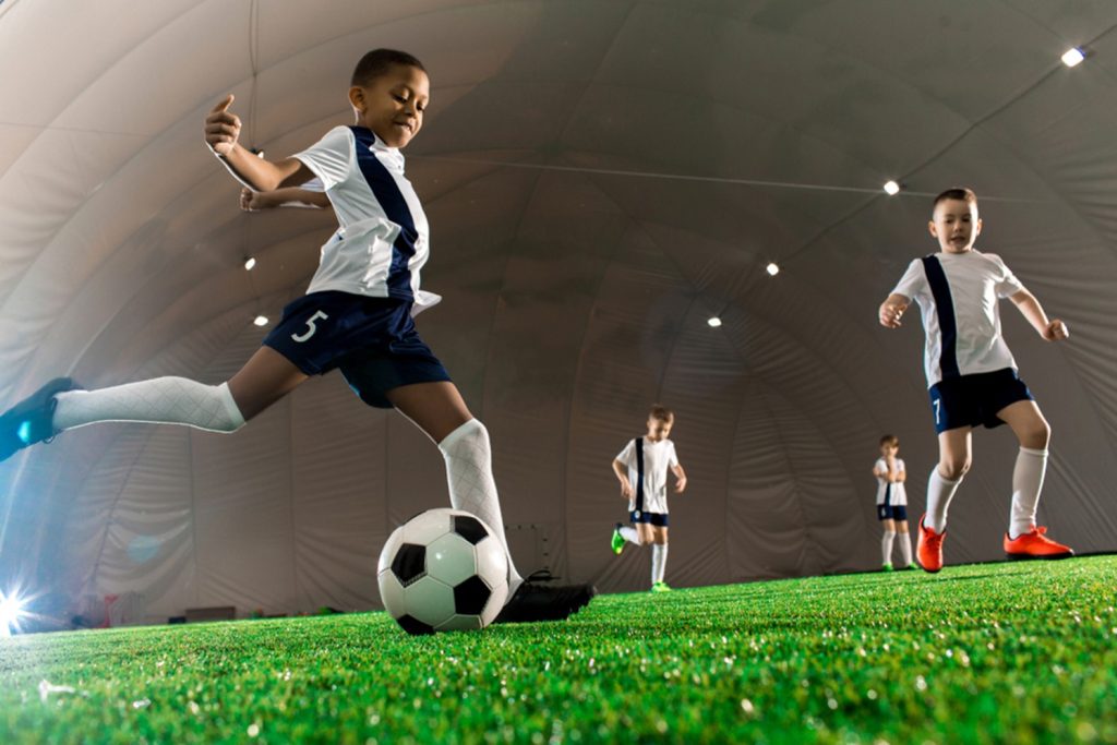 young kid kicking soccer ball with teammates