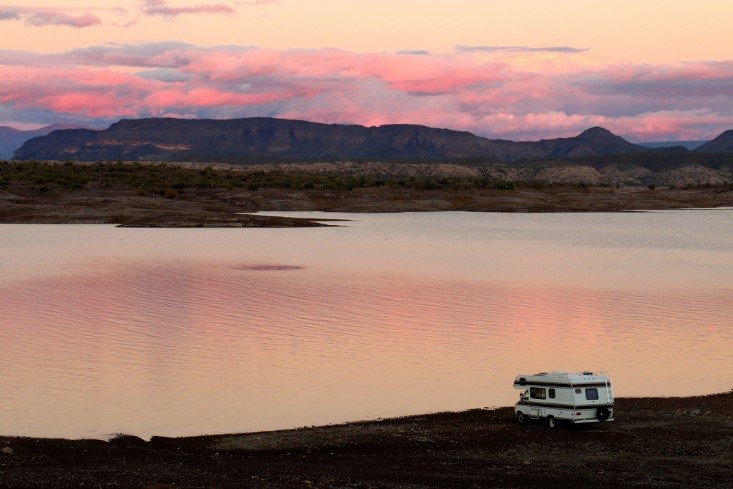 rv on bank of lake during sunset with mountains in background