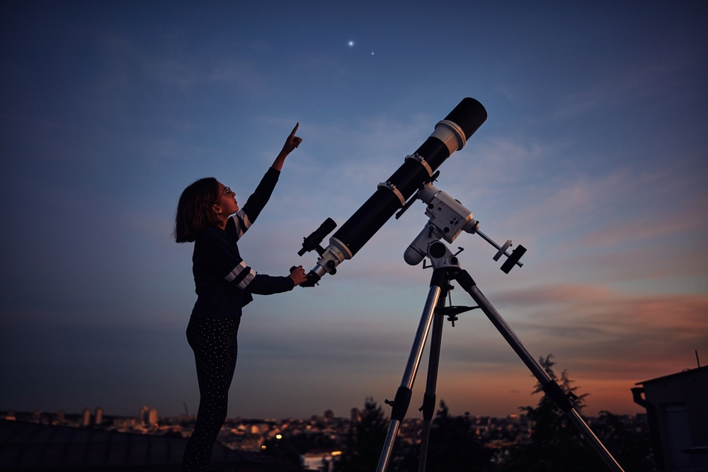 Girl pointing at a starry night with her telescope